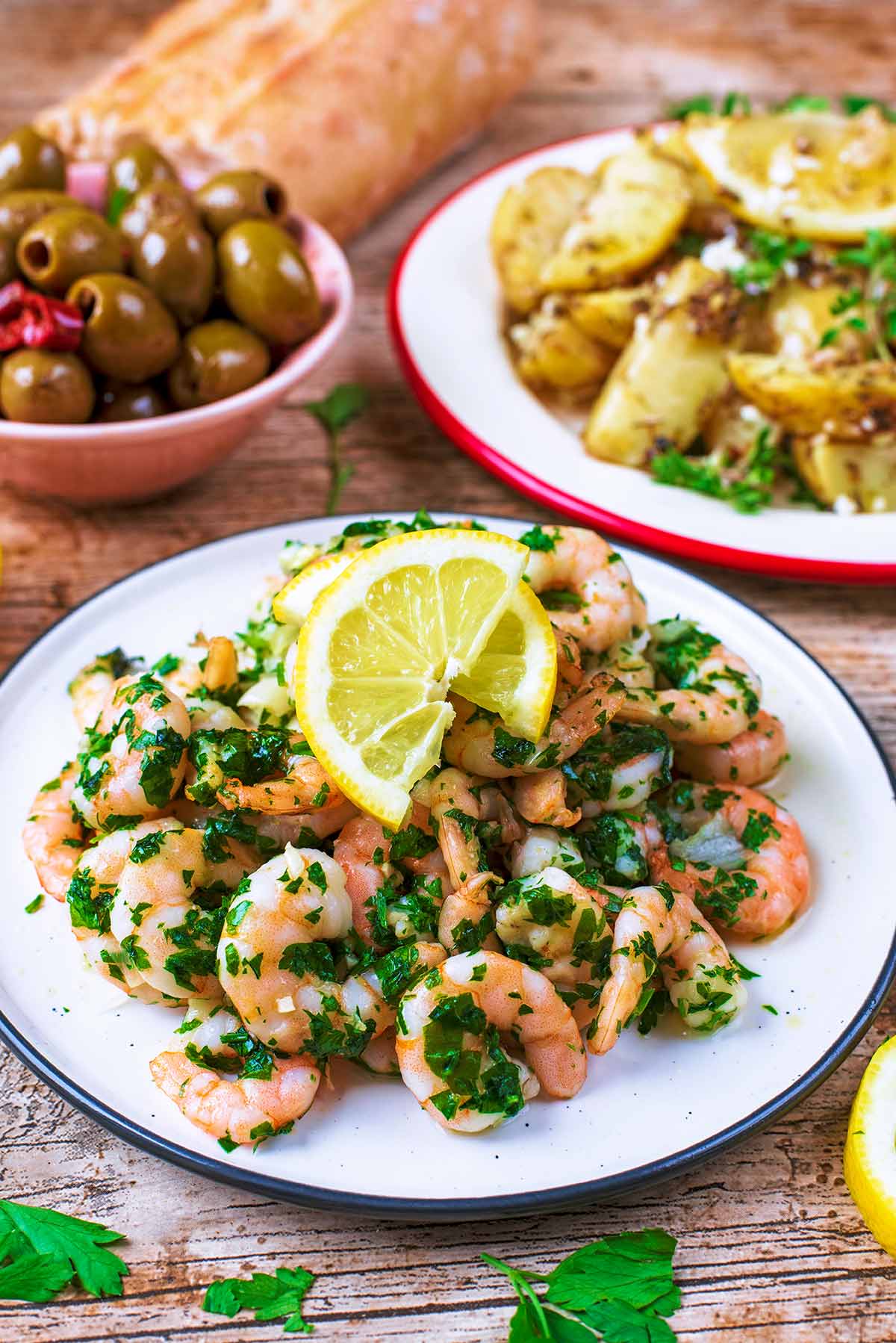 Cooked King Prawns on a white plate. olives and potatoes are in the background.