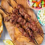 Greek lamb souvlaki skewers on a wooden board.