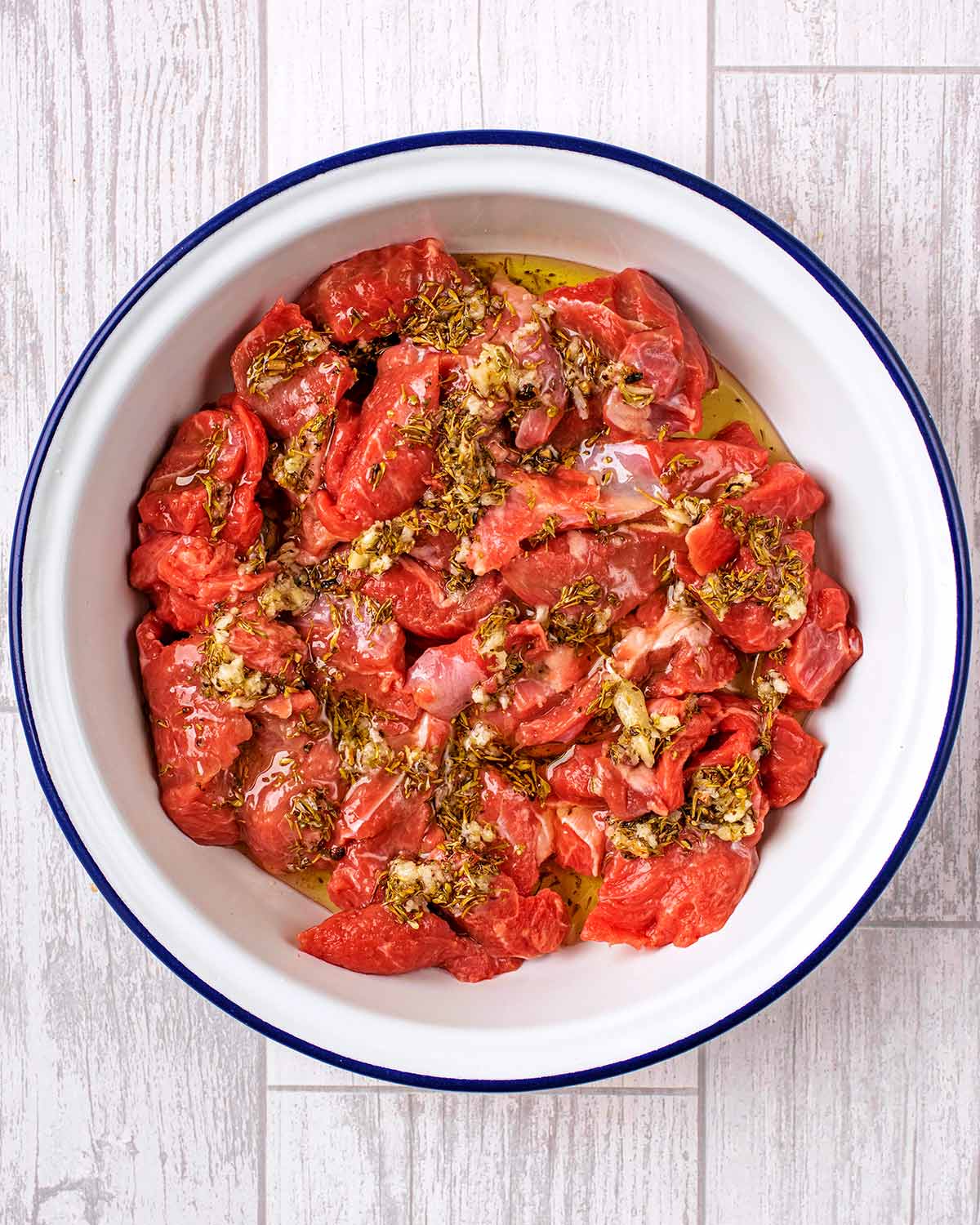 Chunks of raw lamb in a bowl with a marinade poured over.