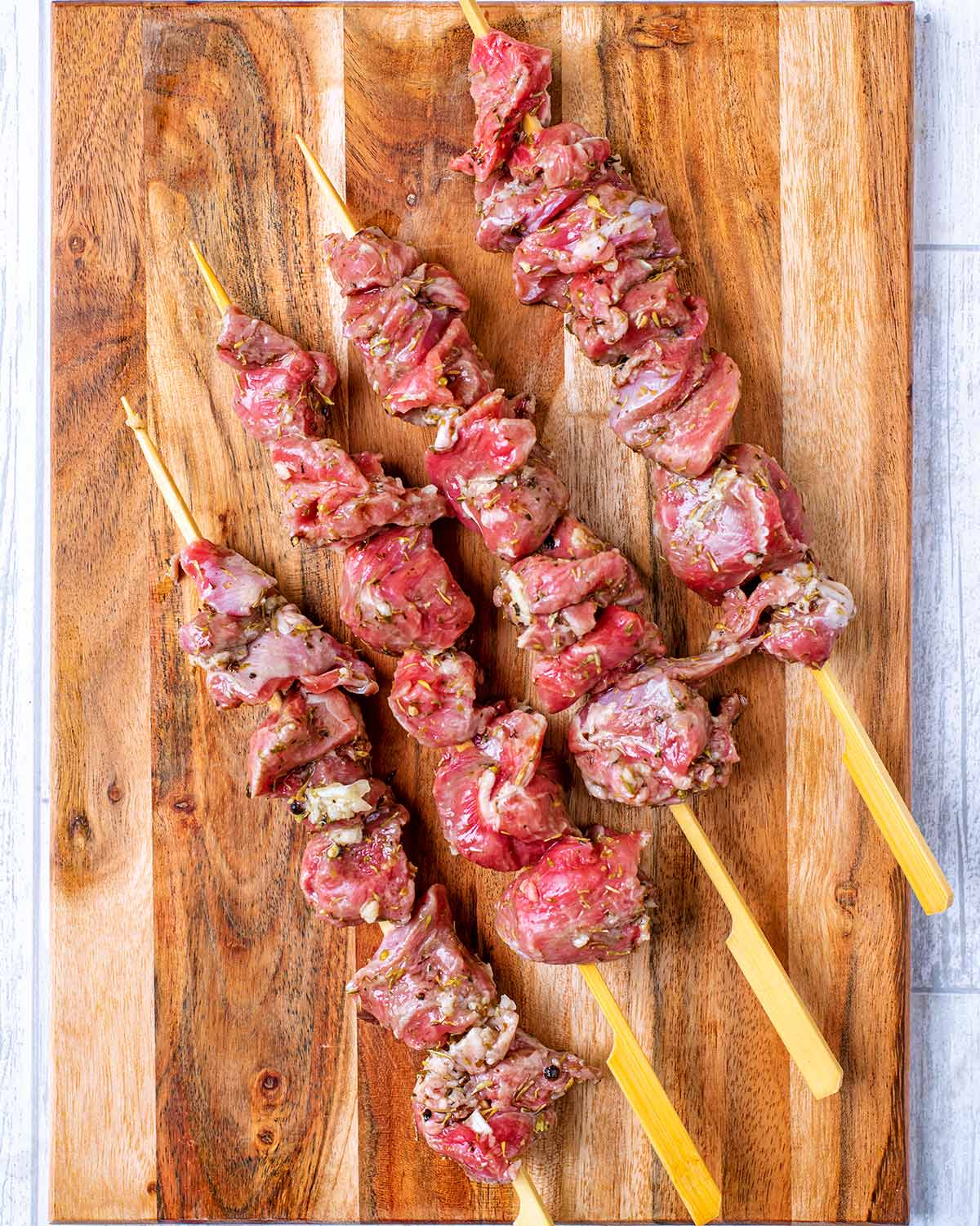 Four wooden skewers with marinated lamb threaded onto them.