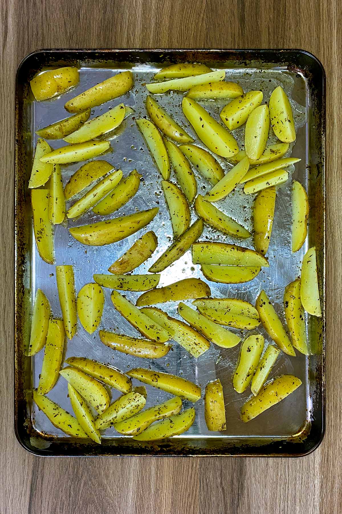 Seasoned potato wedges spread over a baking tray.