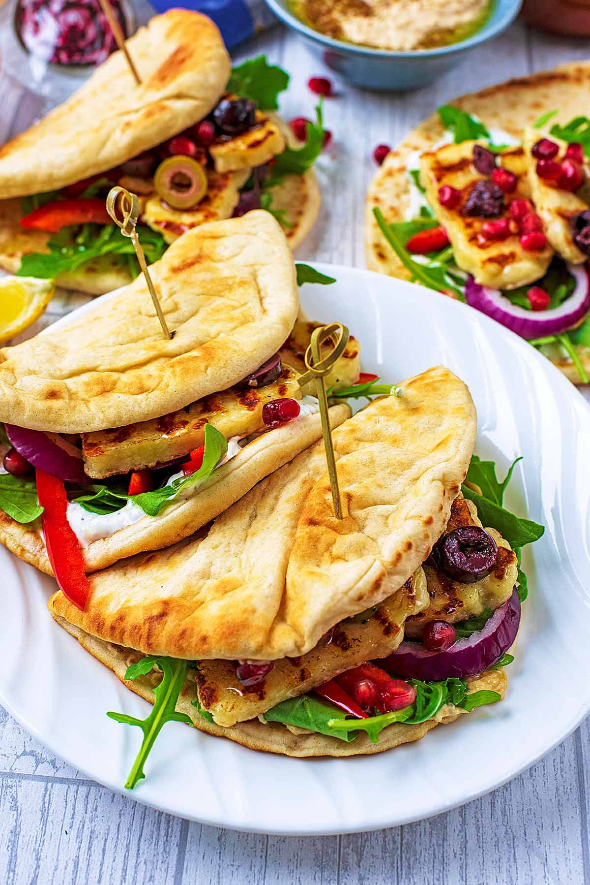 Two halloumi flatbreads on a white plate with more filled flatbreads in the background.