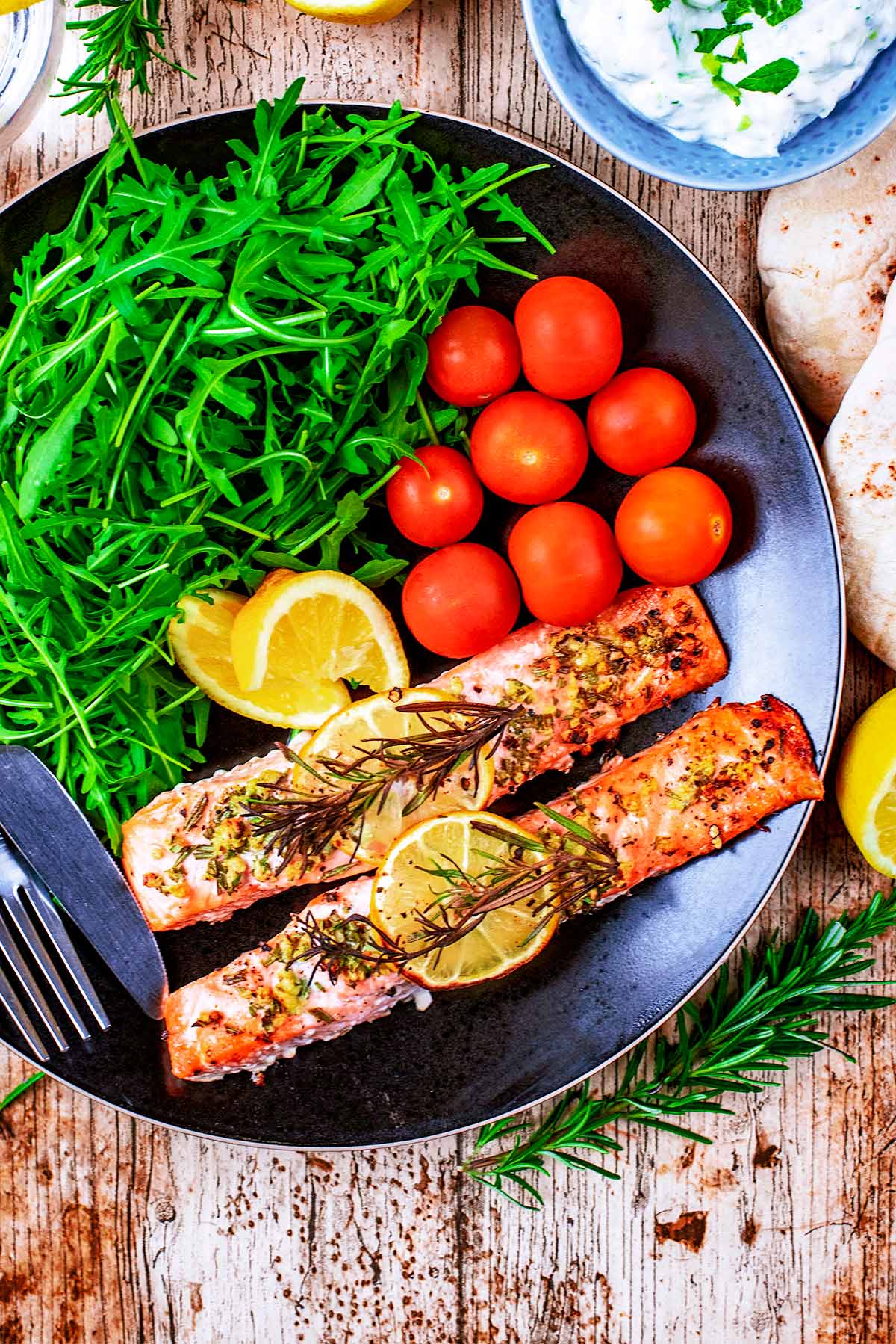 Cooked salmon fillets on a black plate with tomatoes and salad.