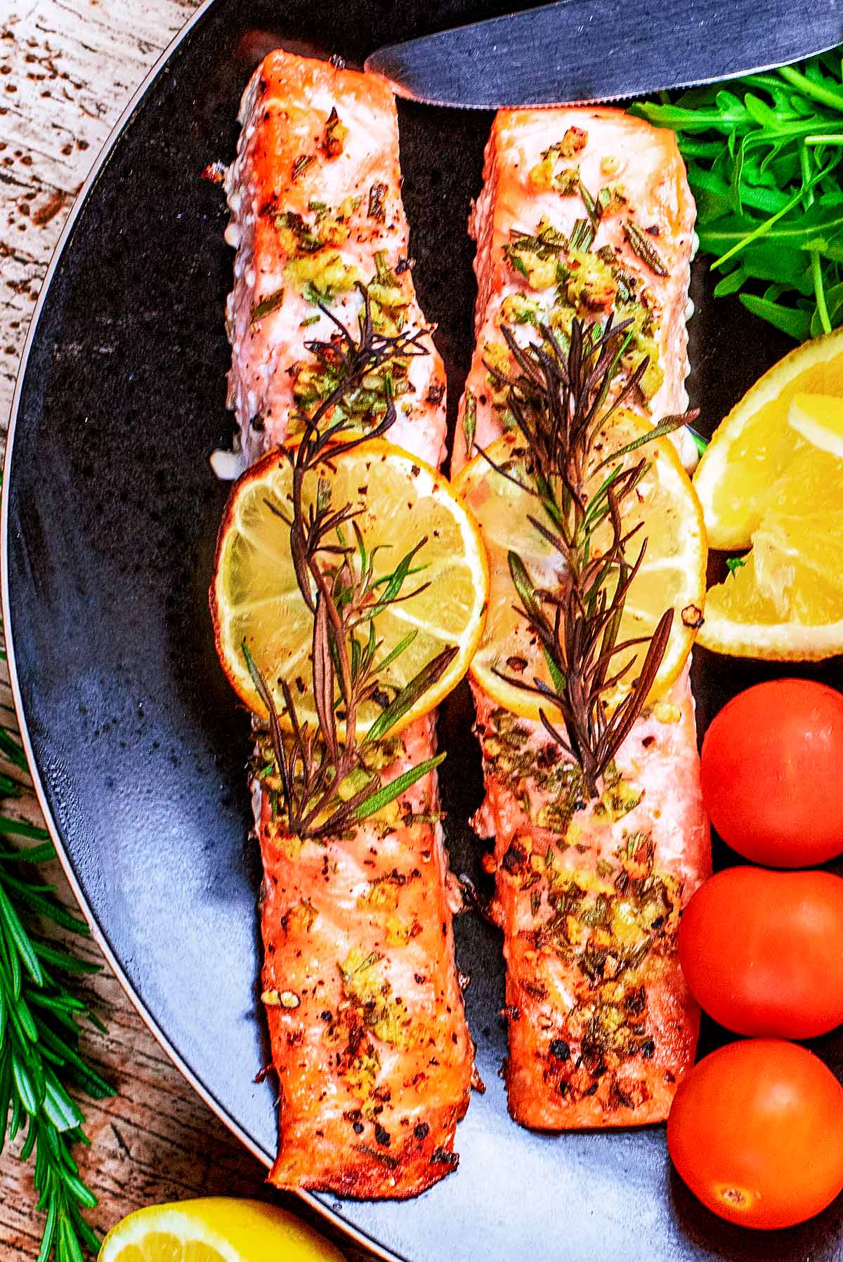 Two cooked salmon fillets with lemon slices on top of them.