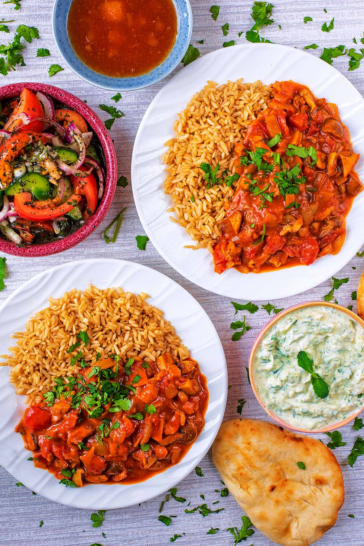 Two plates of Mushroom Curry next to a small mint salad and a bowl of raita.
