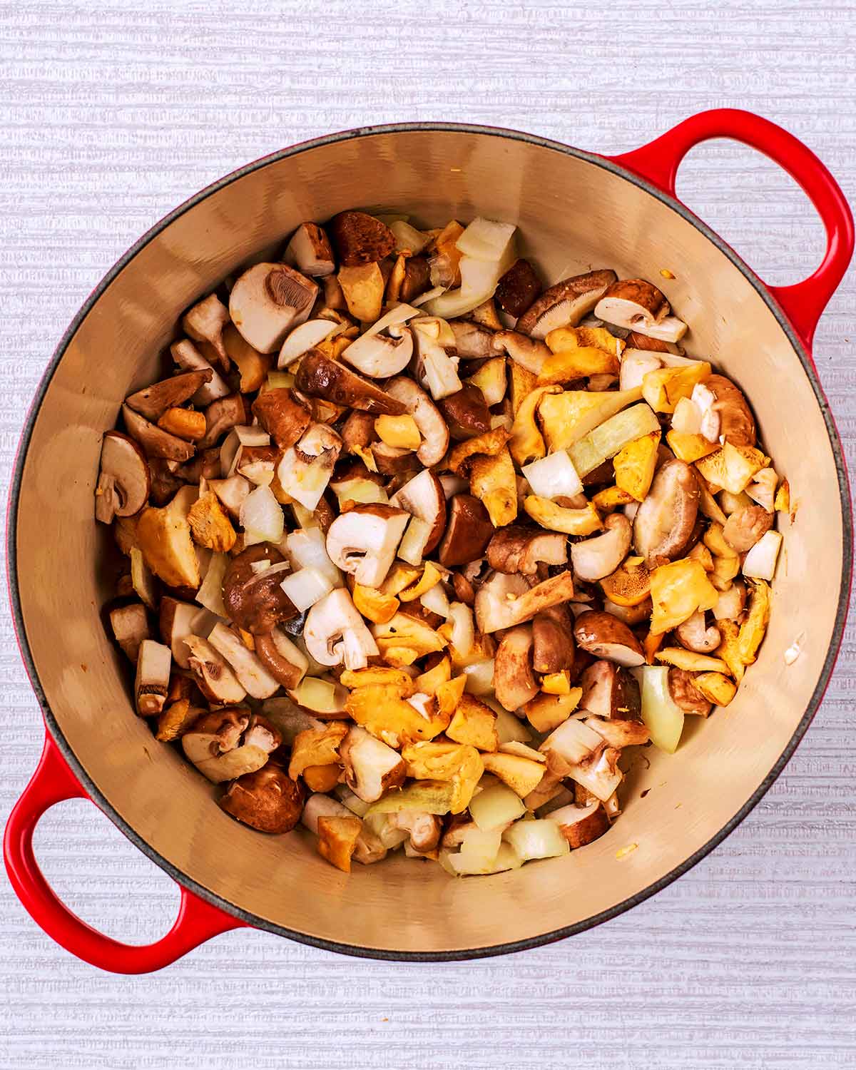 A large pan with chopped mushrooms and onions cooking in it.