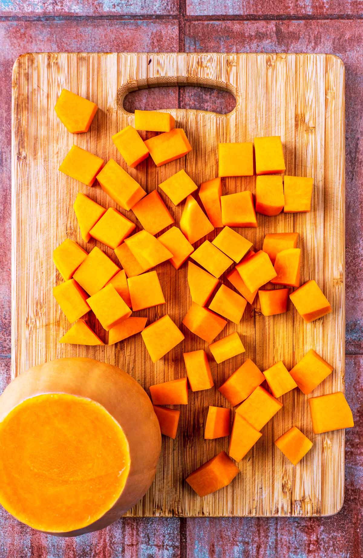 A chopping board with half a butternut squash and cubes of diced butternut squash.