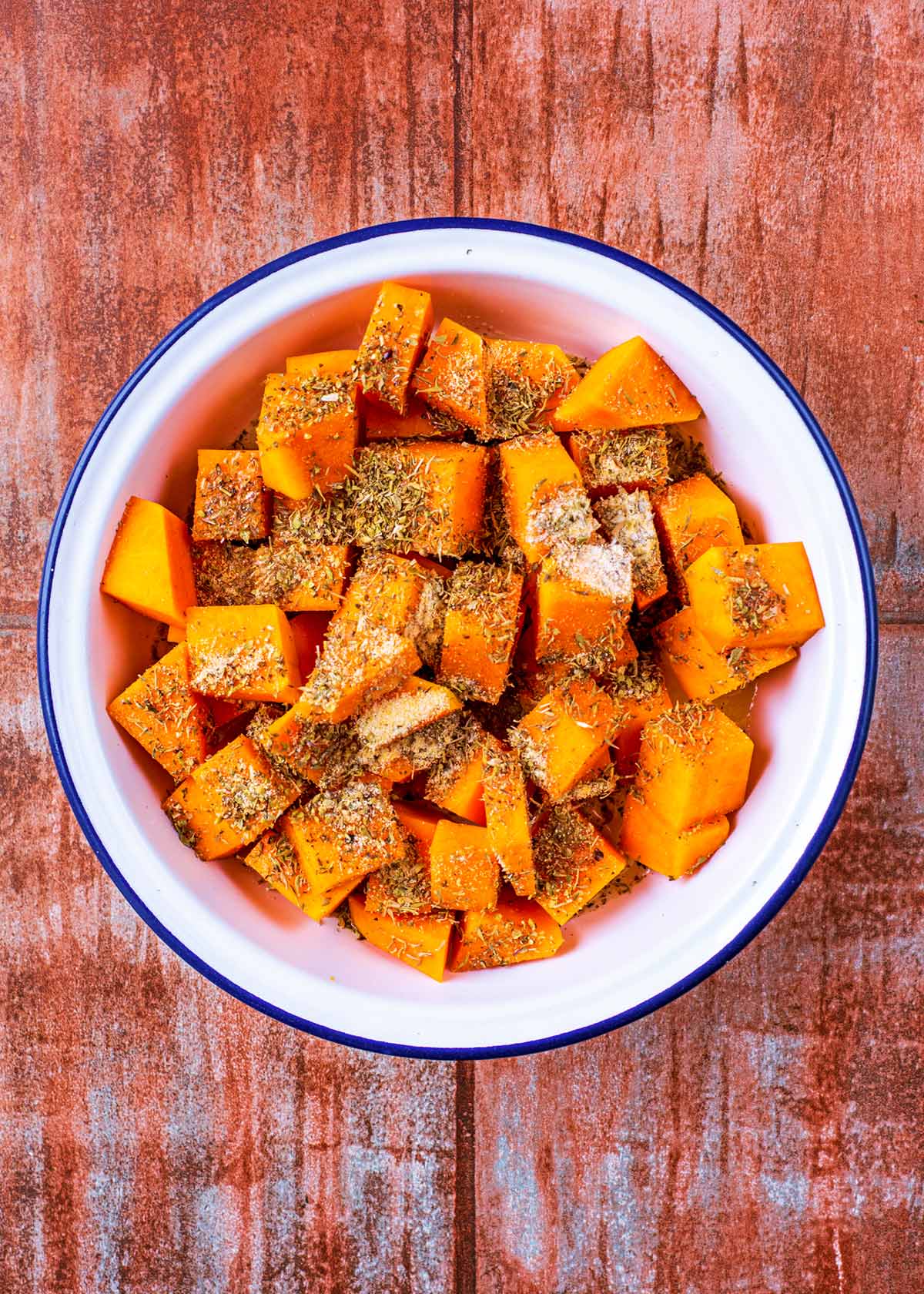 A white bowl containing seasoned cubes of butternut squash.
