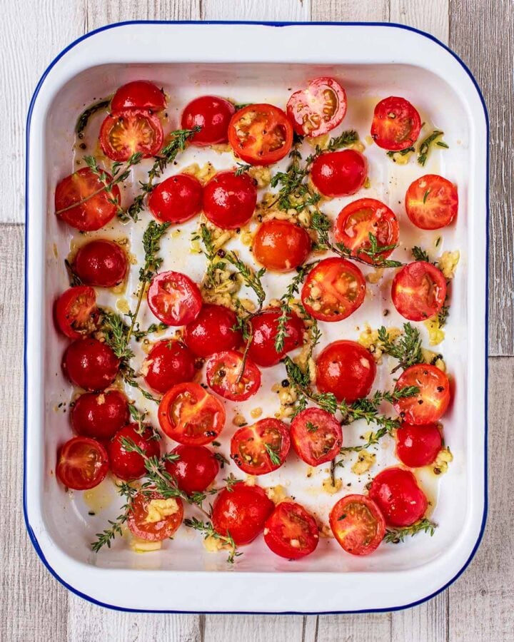 Halved cherry tomatoes, oil and sprigs of thyme in a baking tray.