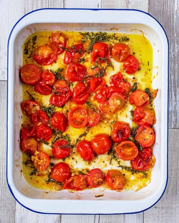 Cooked cherry tomatoes that have burst open in a baking tray with cooked sprigs of thyme.