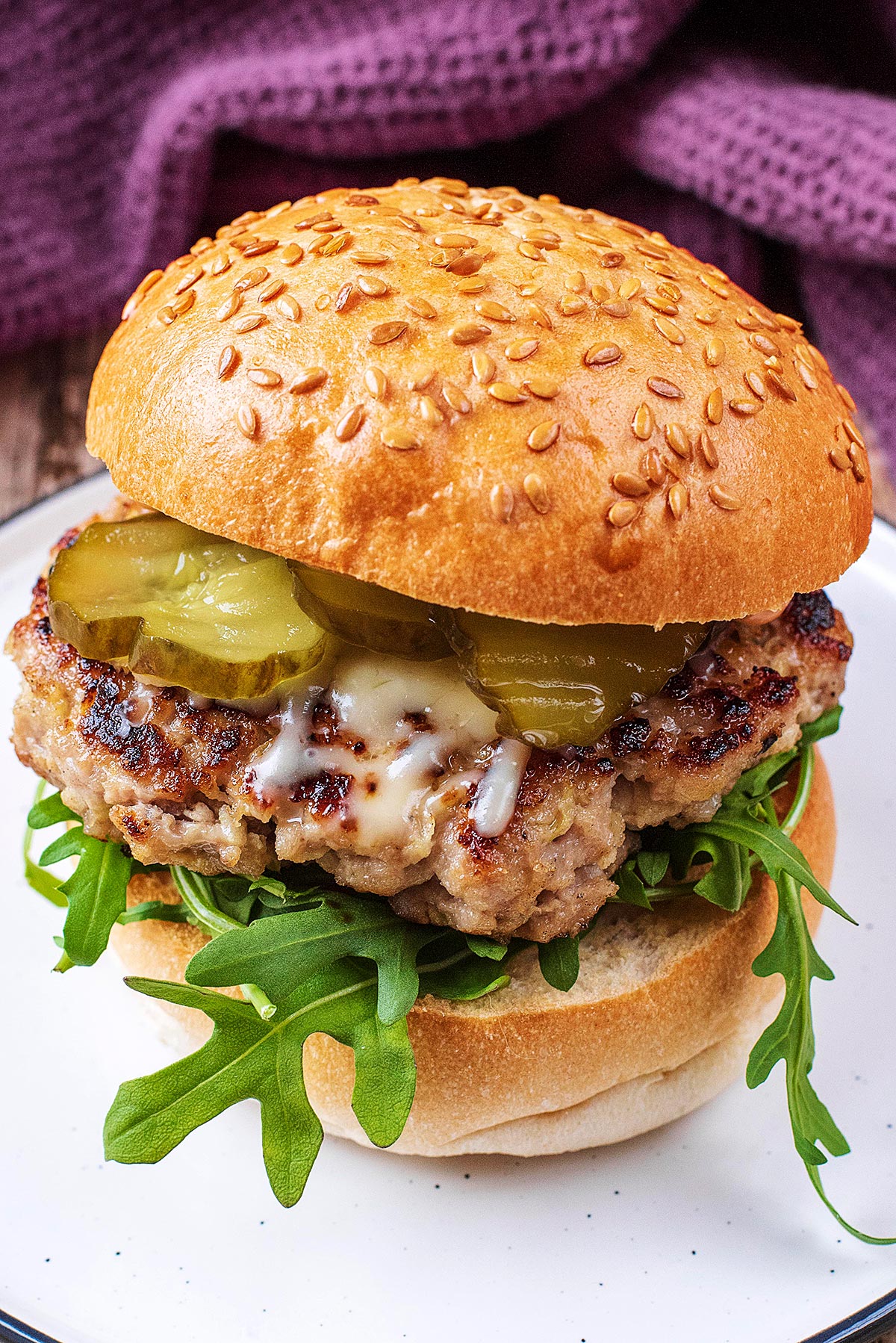 A burger in a sesame seed bun with lettuce leaves, pickles and melted cheese.