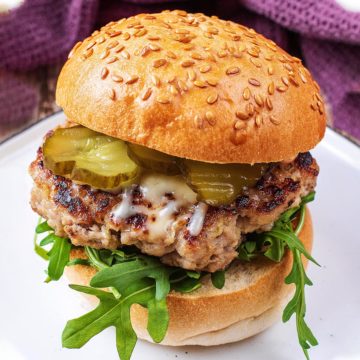 Pork and apple burger in a sesame seed bun with lettuce and pickles.