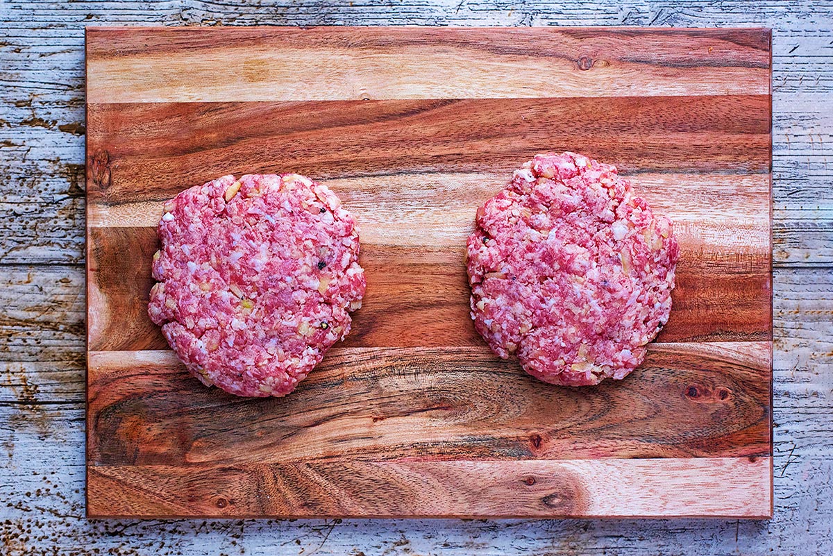Two burger patties on a wooden chopping board