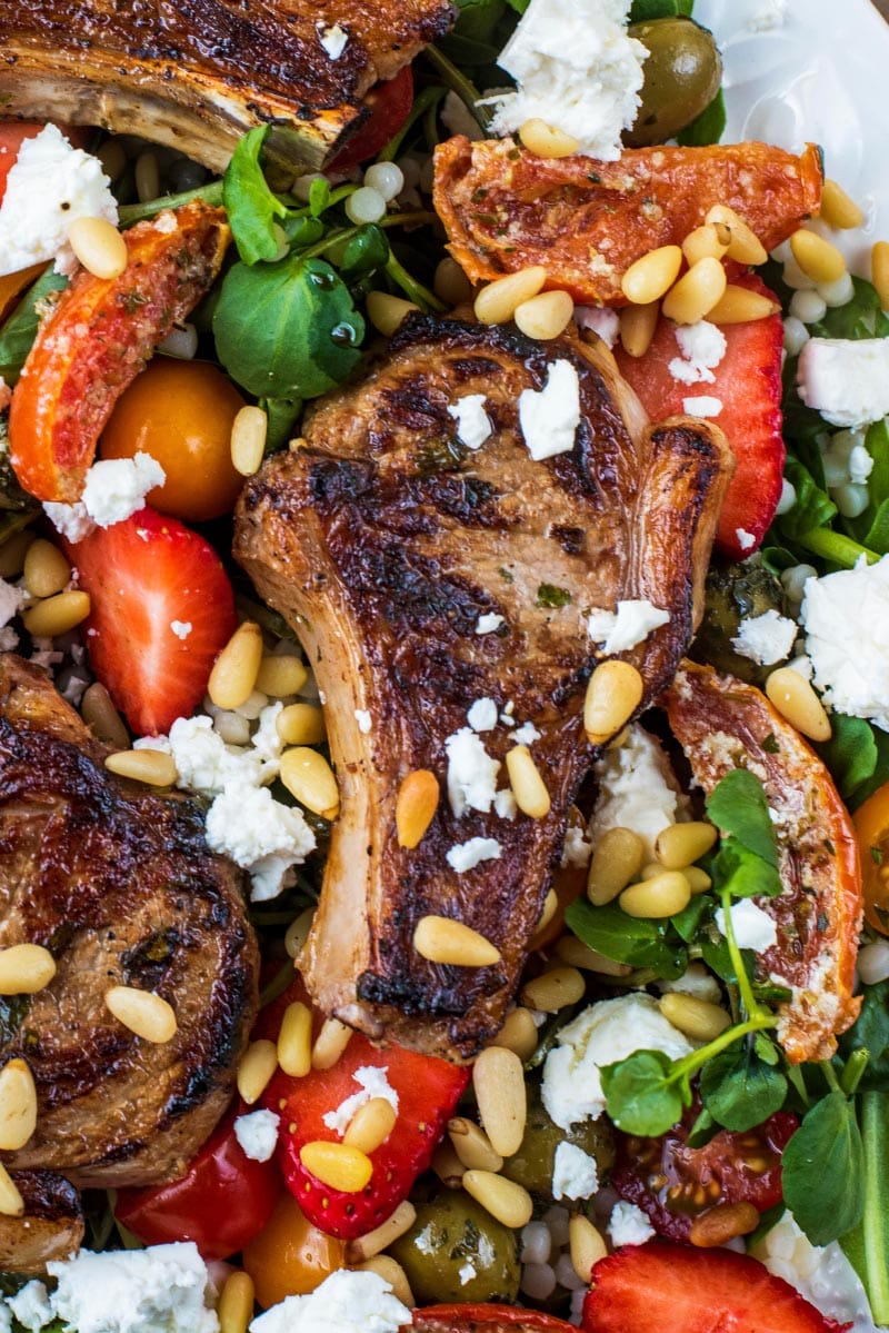 a cooked lamb chop on top of salad, topped with feta and pine nuts.