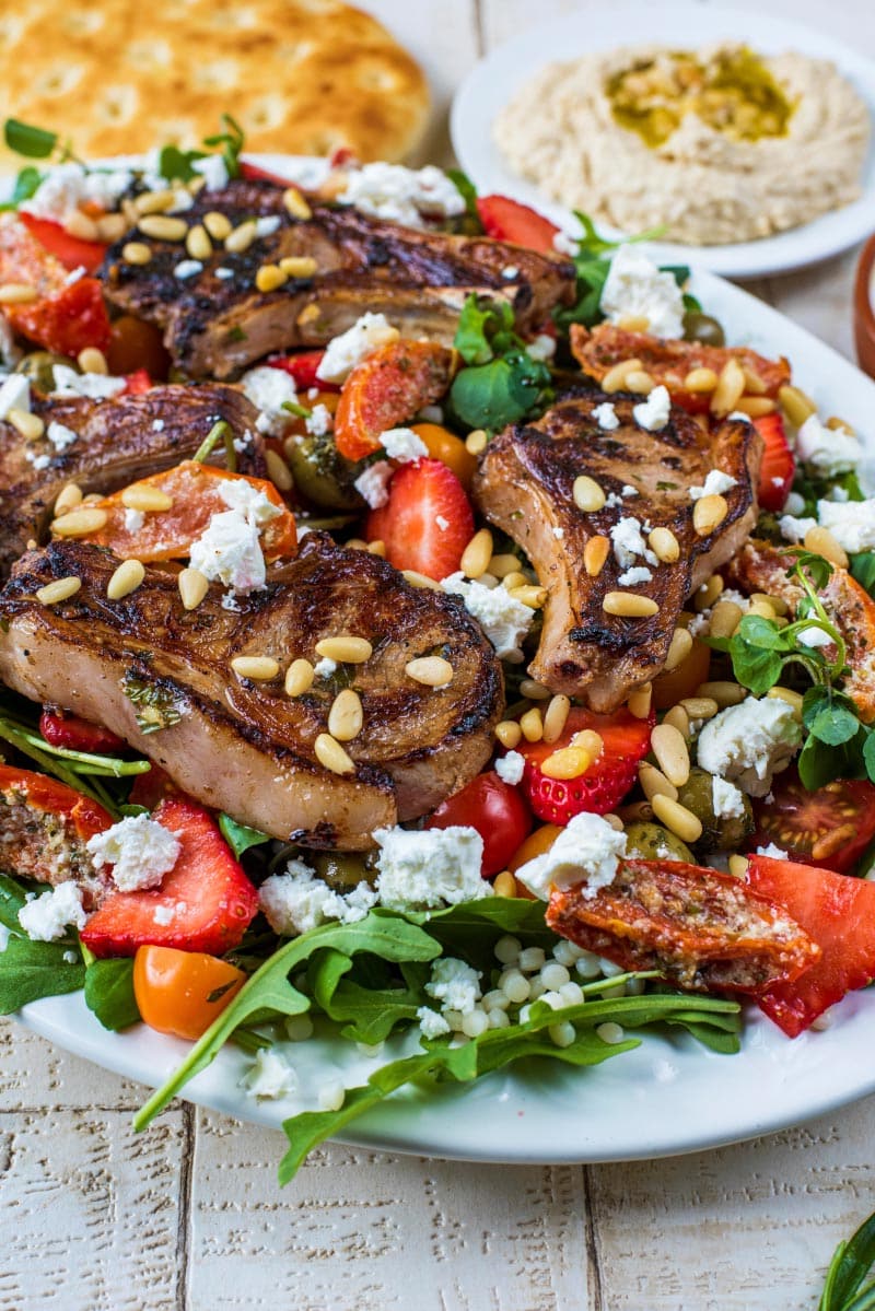 a large plate of salad topped with lamb chops.