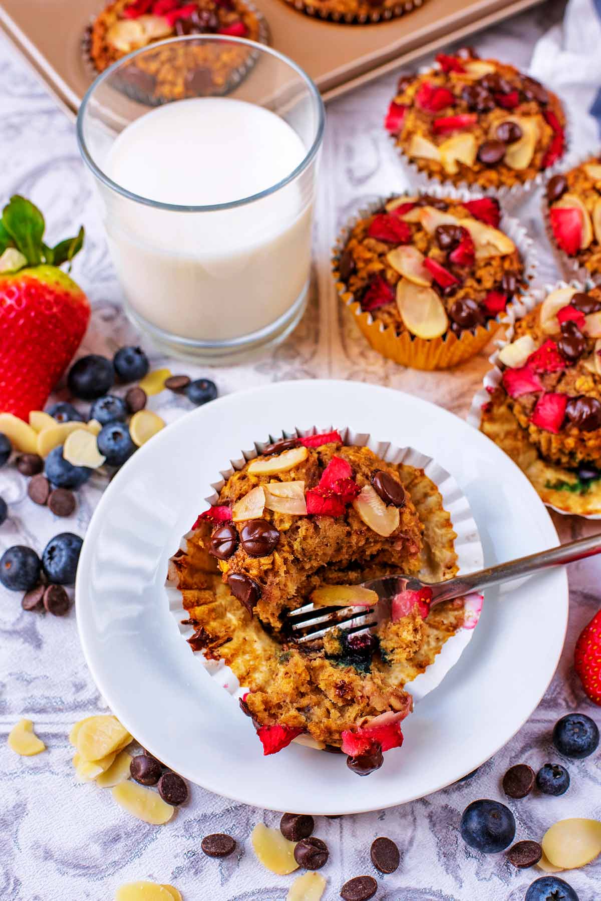 A banana oat muffin on a plate in front of a glass of milk and some more muffins.