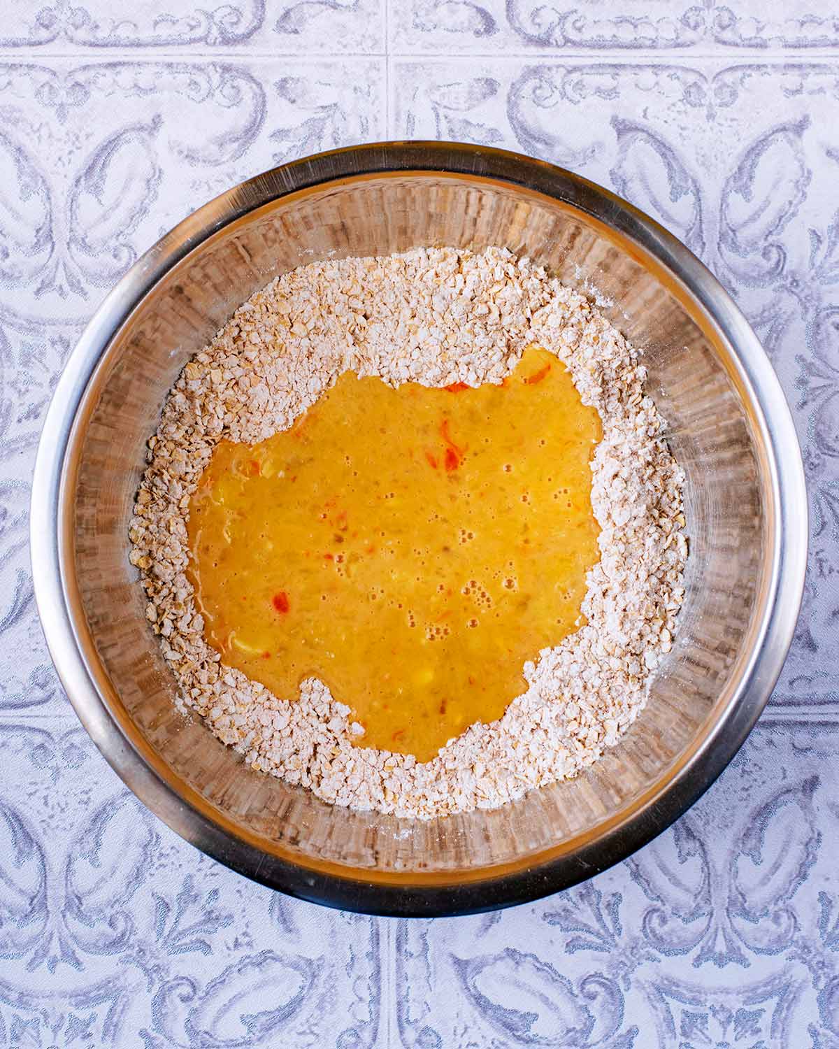 Oats and flour in a bowl with whisked eggs poured on top.