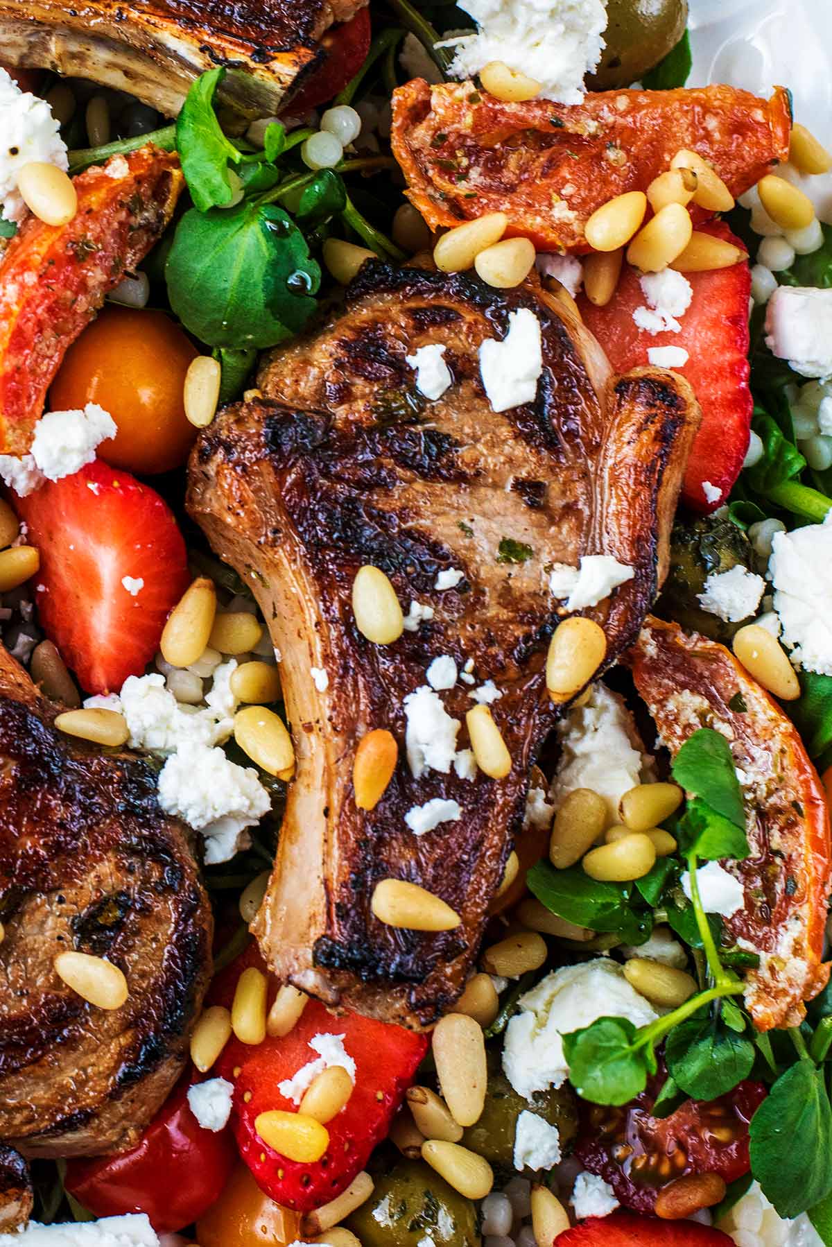 a cooked lamb chop on top of salad, topped with feta and pine nuts.