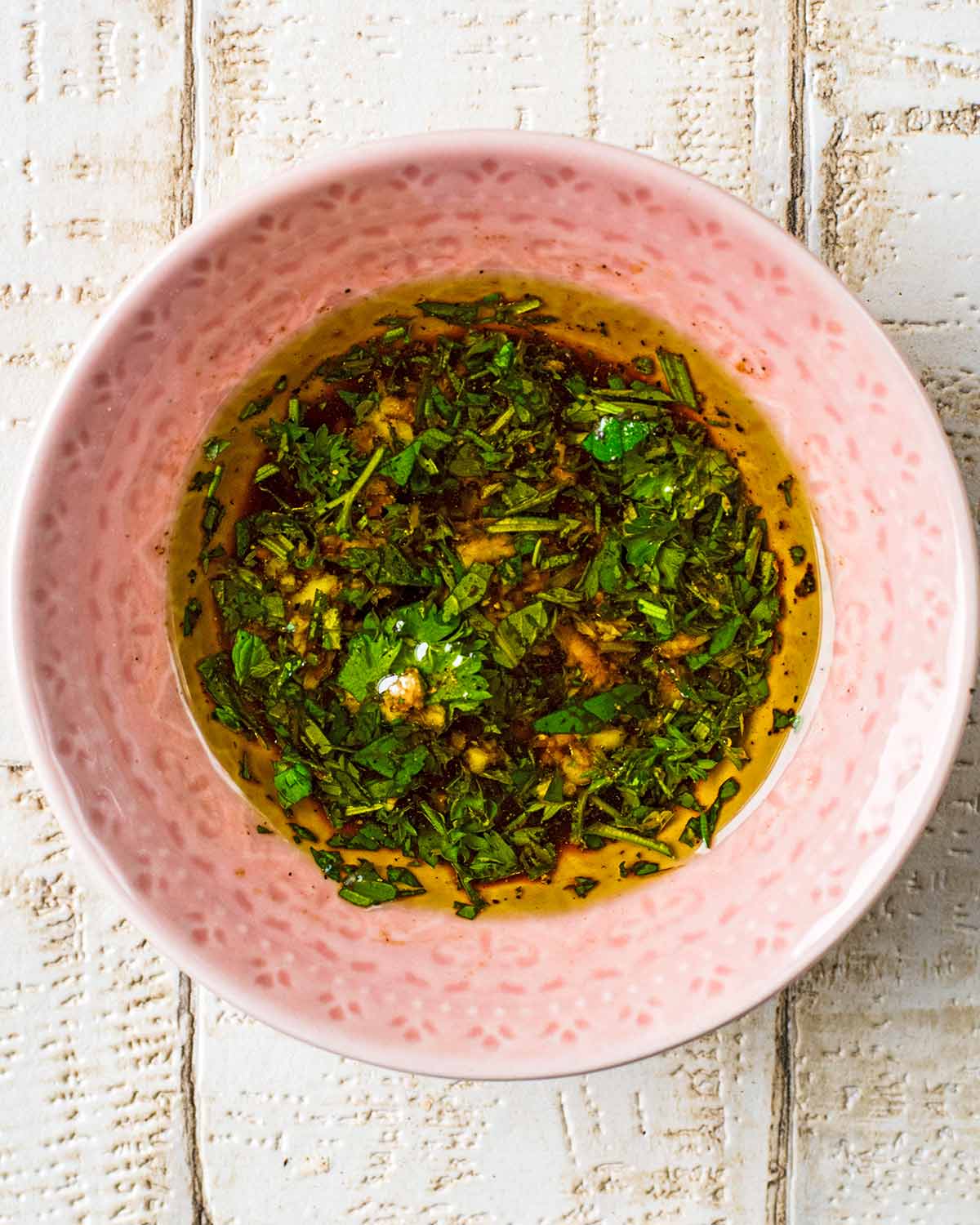 A small pink dish containing an oil and herb based salad dressing.