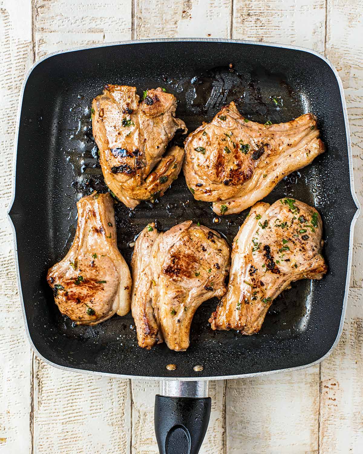 Five lamb chops frying in a griddle pan.