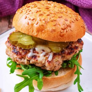 Pork and apple burger in a sesame seed bun with lettuce and pickles.