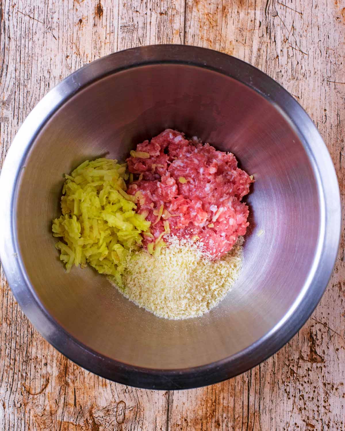 A bowl containing pork mince, grated apple and breadcrumbs.