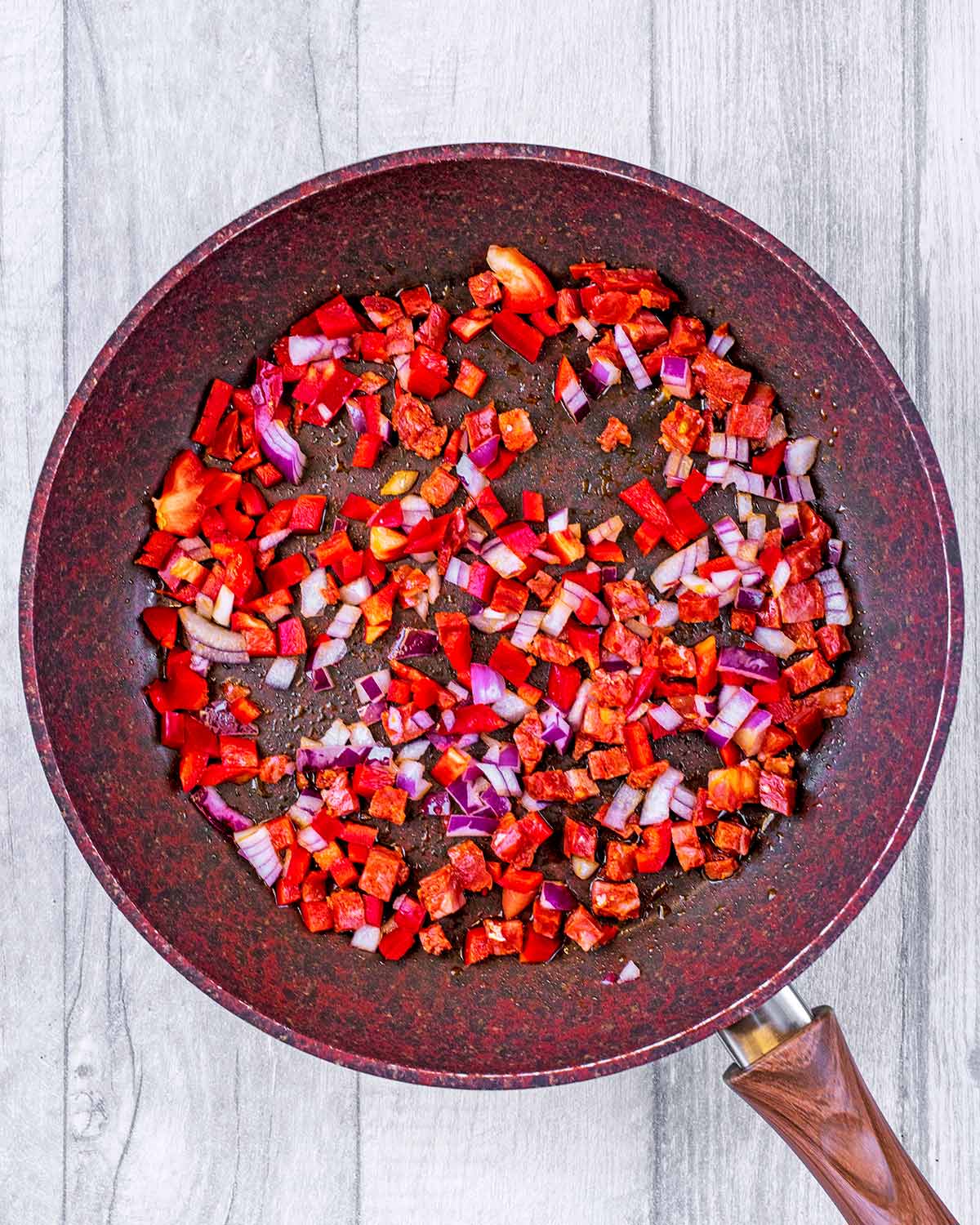 A frying pan with chopped red pepper and red onion.
