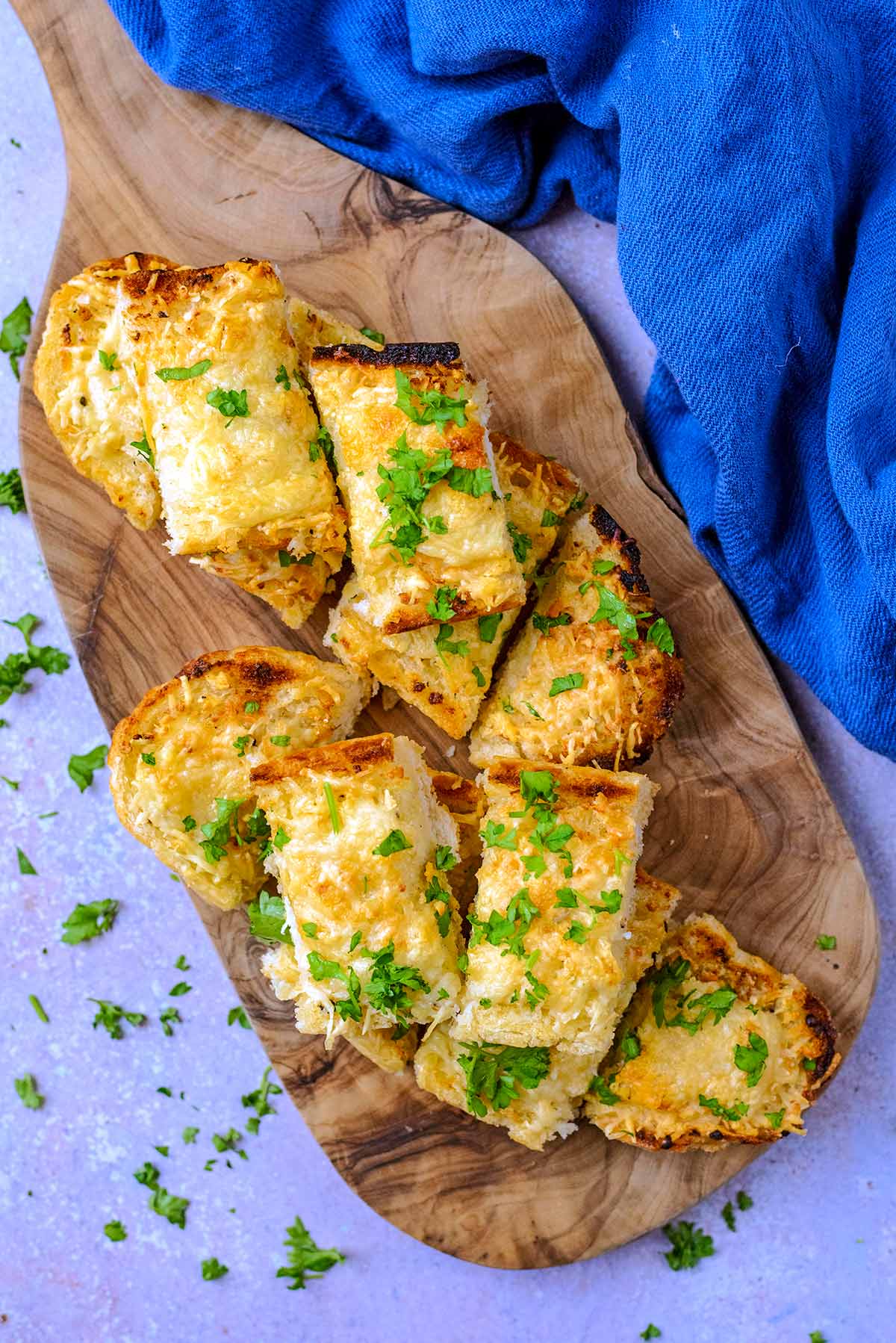 Slices of cheese topped garlic bread on a wooden serving board.