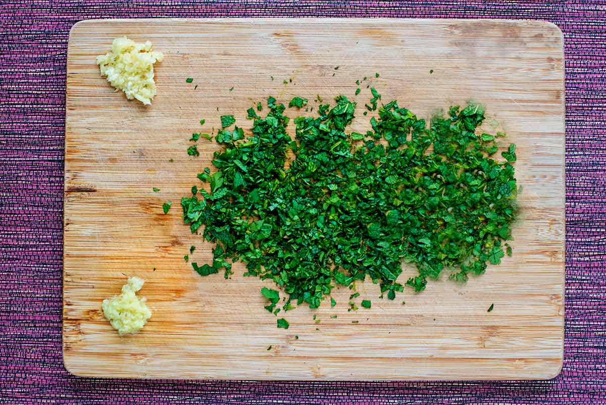 A chopping board with chopped mint, crushed garlic and grated ginger.