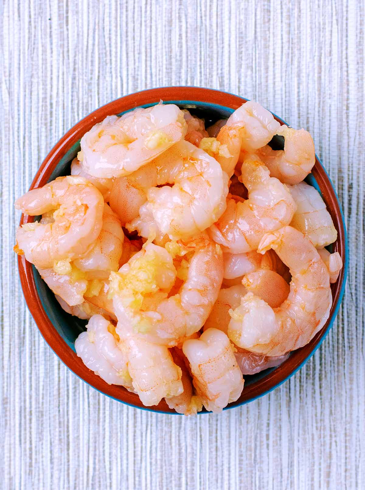 Prawns mixed with oil and garlic in a small bowl.