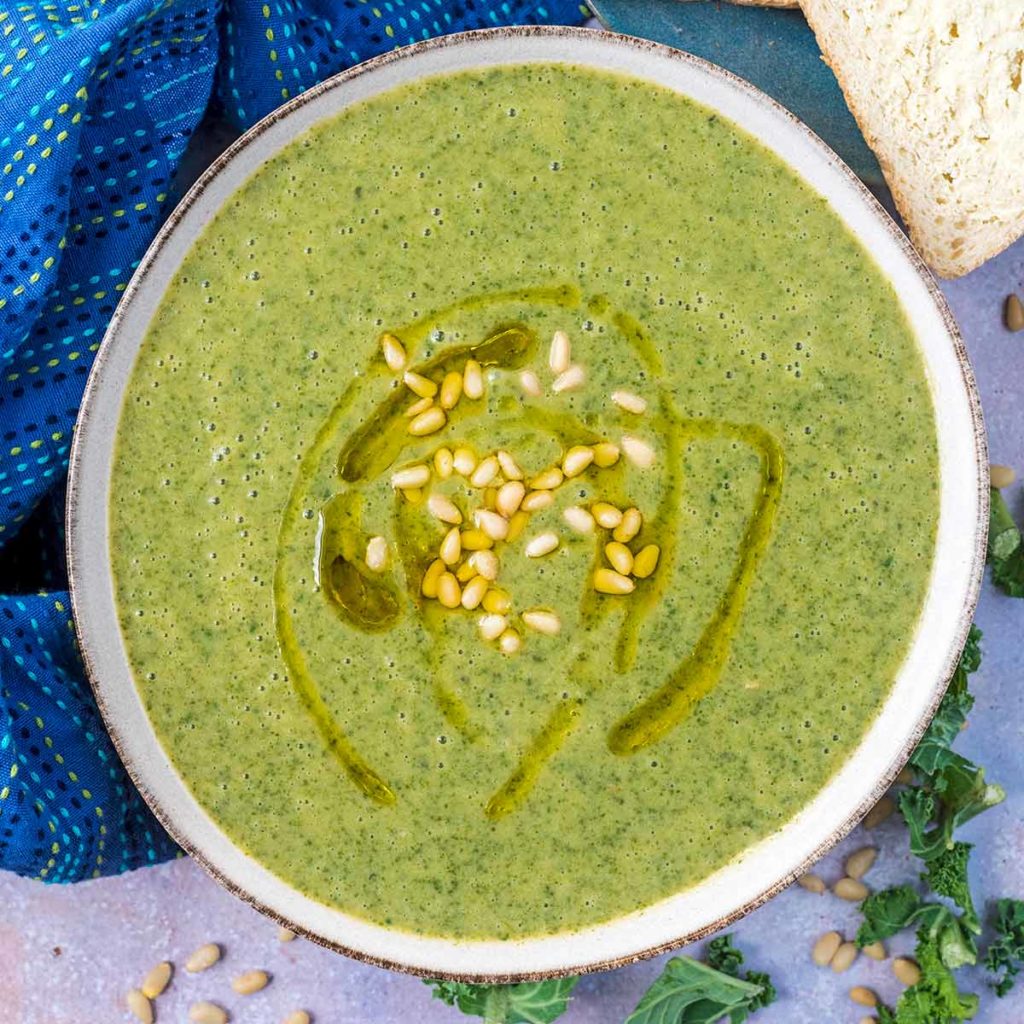 A bowl of kale soup next to some buttered bread.