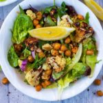 Roasted Cauliflower Salad in a white bowl, surrounded by lemon wedges and chickpeas