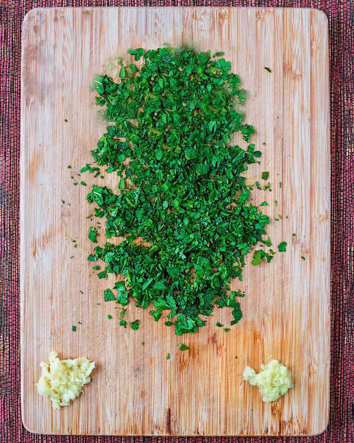 A chopping board with chopped mint, crushed garlic and grated ginger.