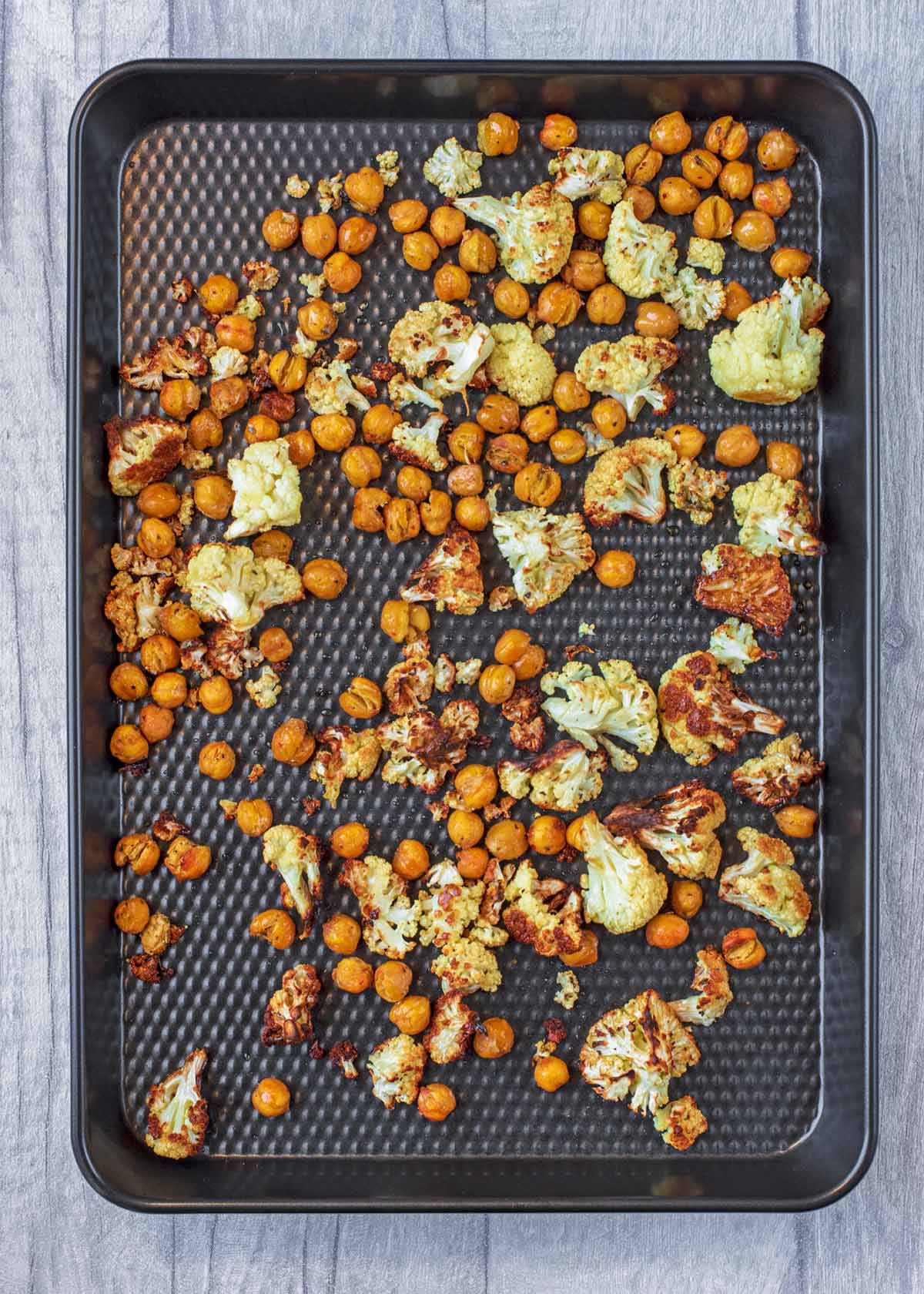A baking tray with the chickpeas and cauliflower now roasted.