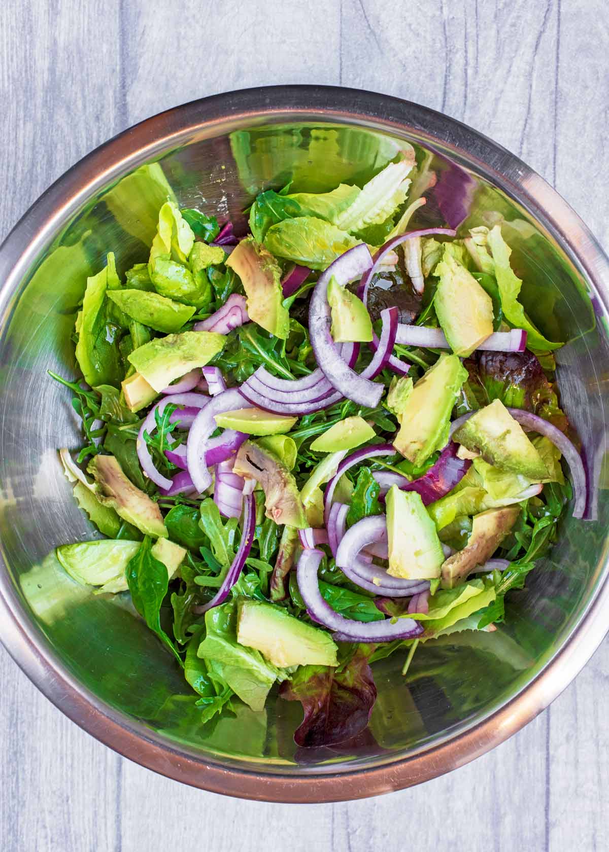 A large mixing bowl containing lettuce leaves, sliced onion and avocado.