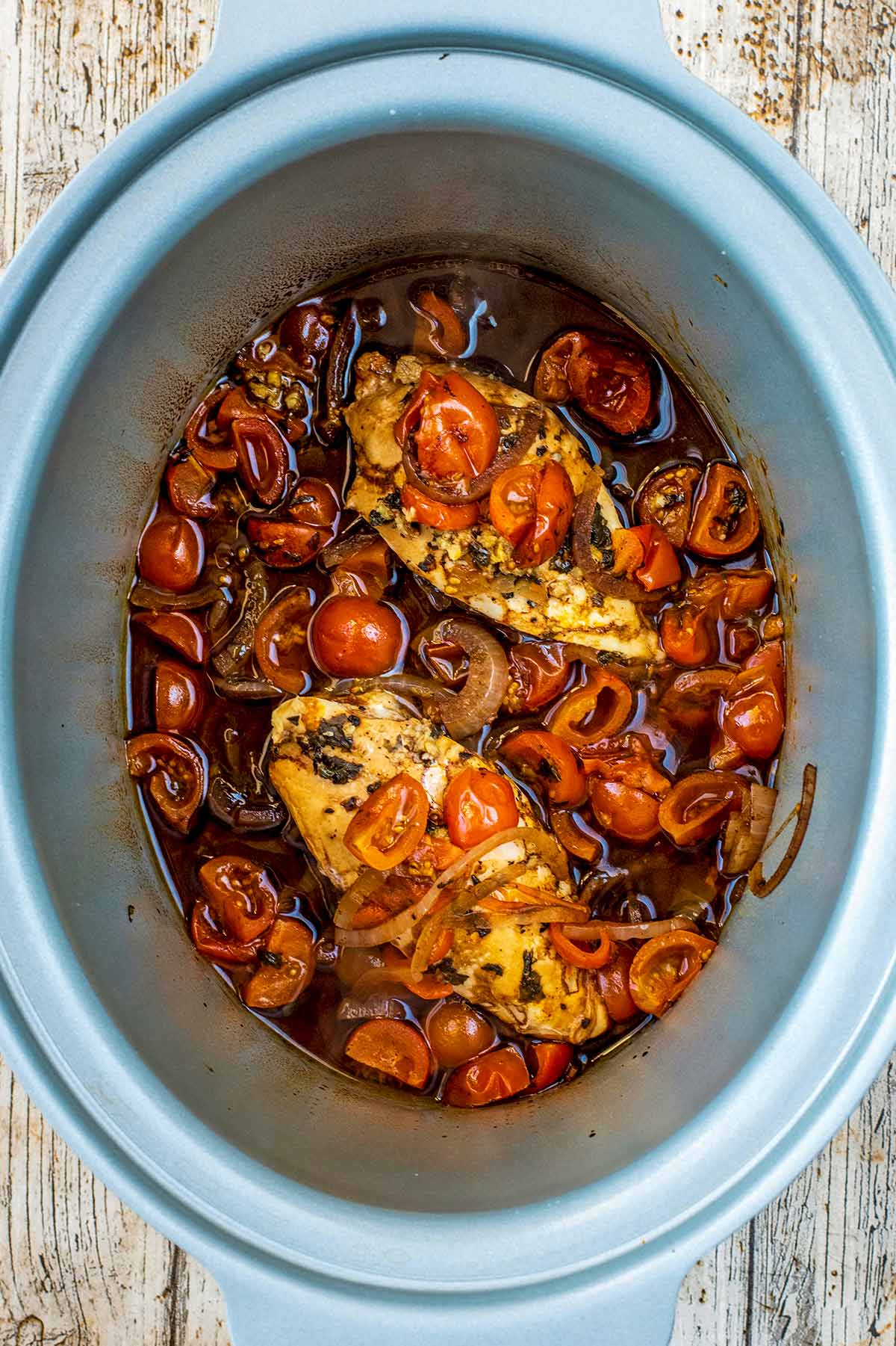 A slow cooker bowl with balsamic chicken, tomatoes and onions.