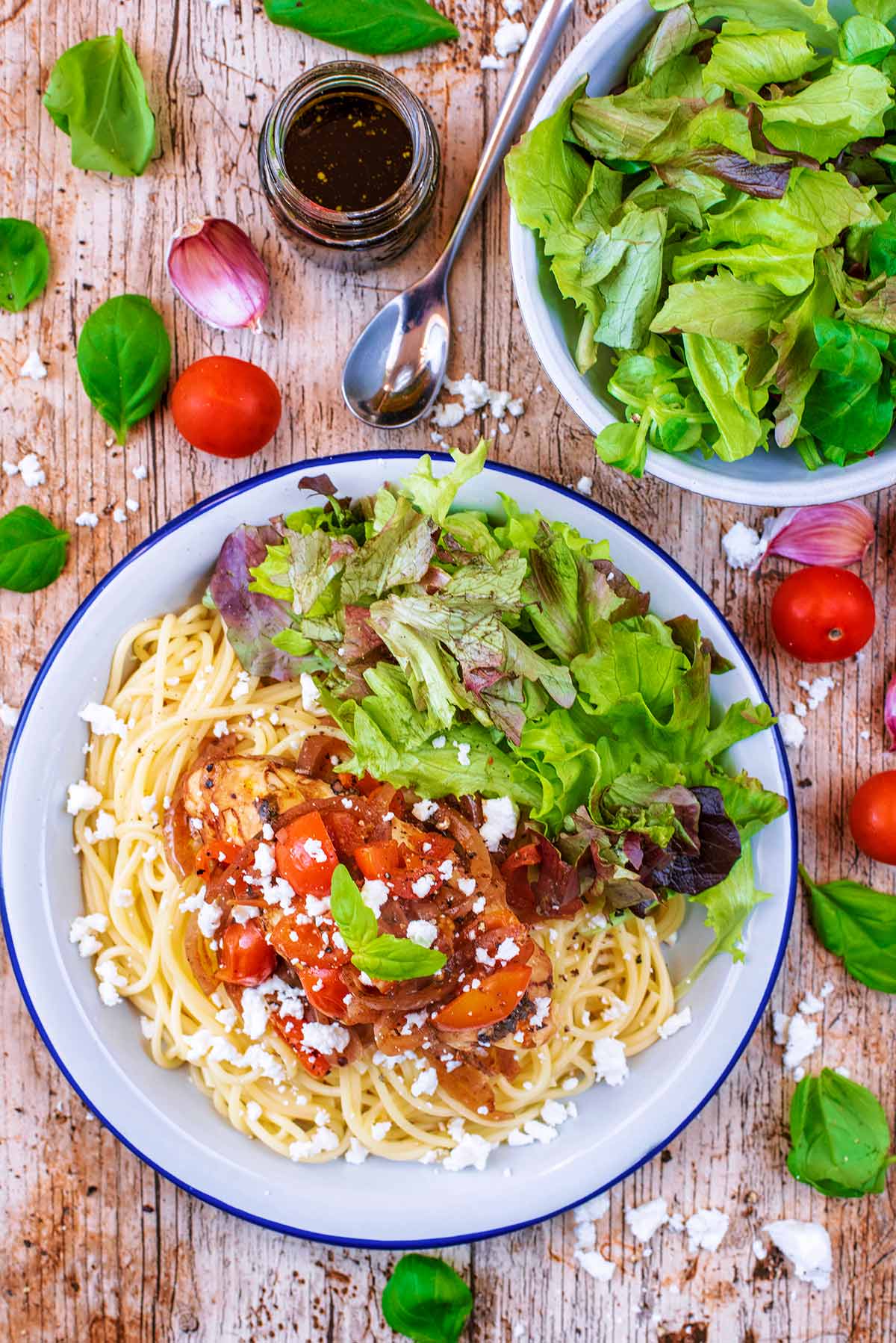Chicken in a sauce on some spaghetti on a plate with salad.