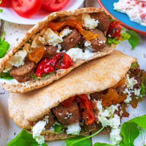 Stuffed lamb pita stacked on top of another next to slaw, salad and tomato slices.