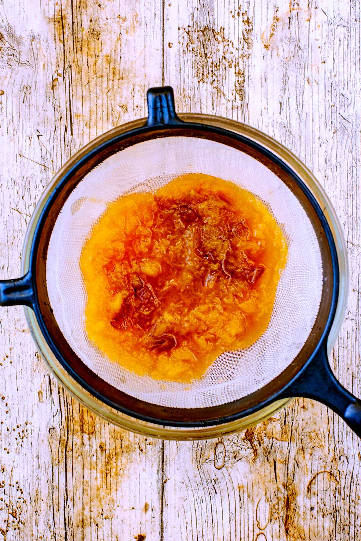 A sieve with peach pulp in it, over a glass bowl.