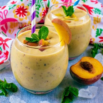 Peach Smoothie in glasses surrounded by mint leaves and peach halves.