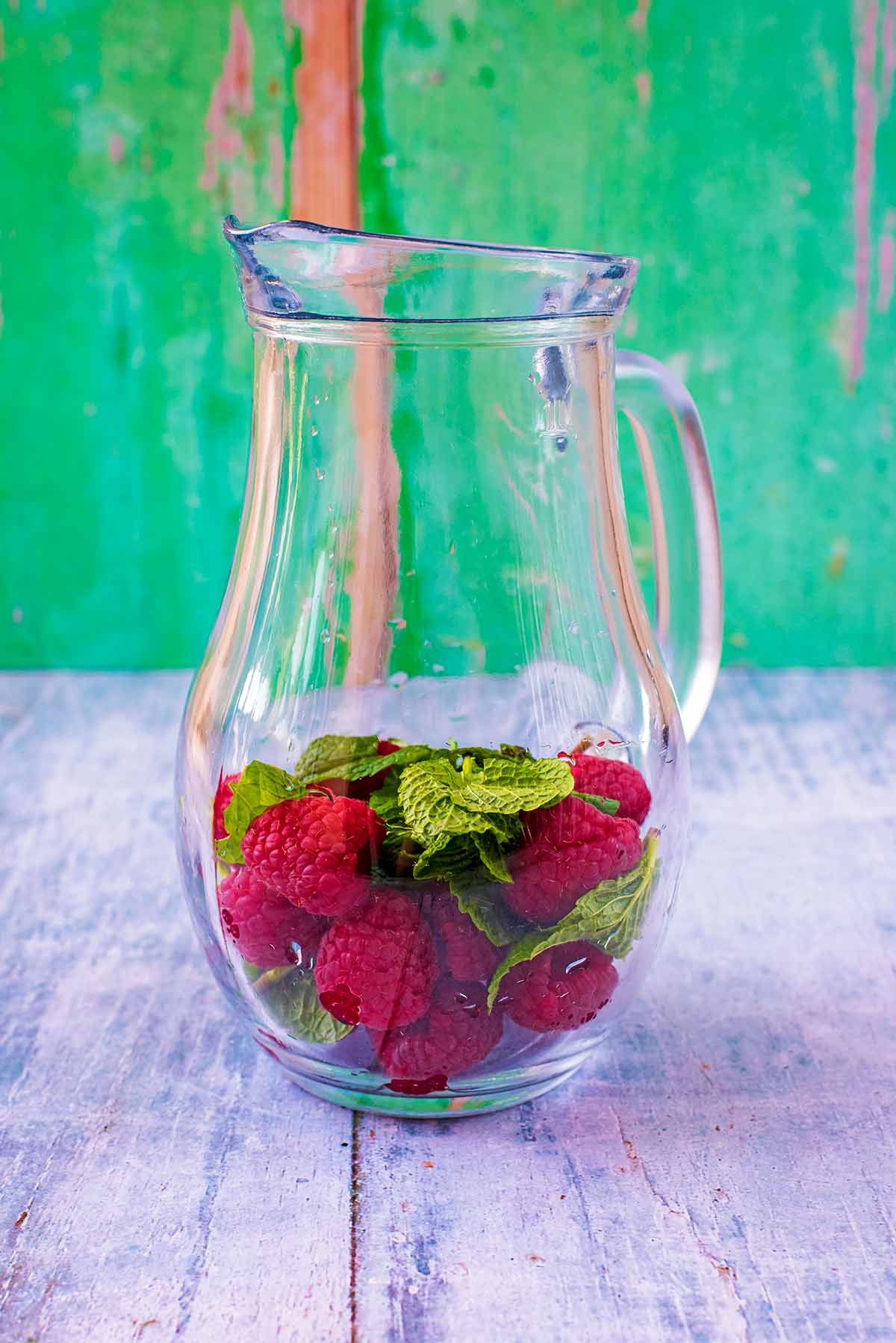 A large glass jug with raspberries and mint leaves in it.