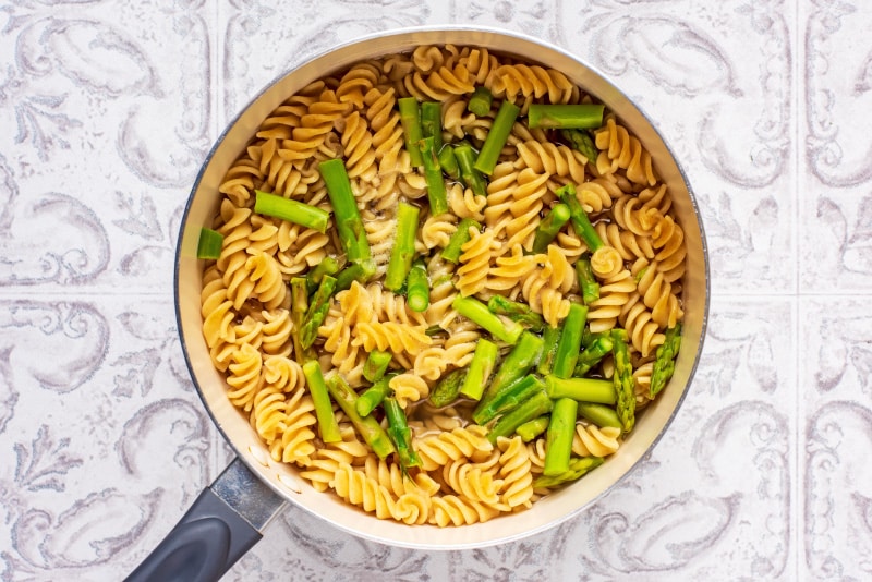 A saucepan containing cooked fusilli pasta and asparagus.