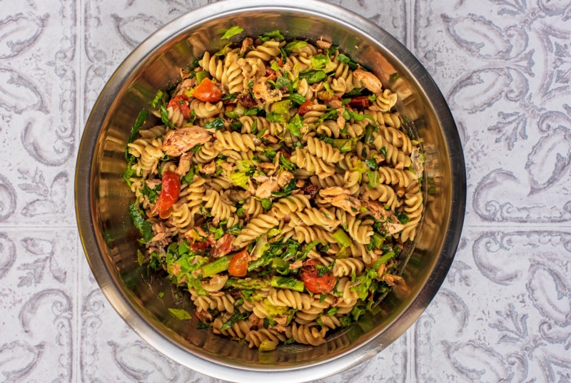 A large metal bowl containing a mixed salmon pasta salad.