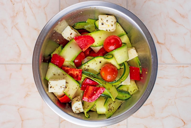 A metal bowl containing chopped vegetables and cubes of halloumi.