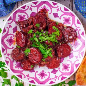 A plate of Chorizo in Red Wine next to some slices of bread.