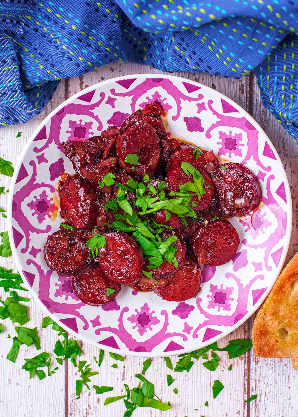 Slices of chorizo in red wine sauce topped with chopped herbs.