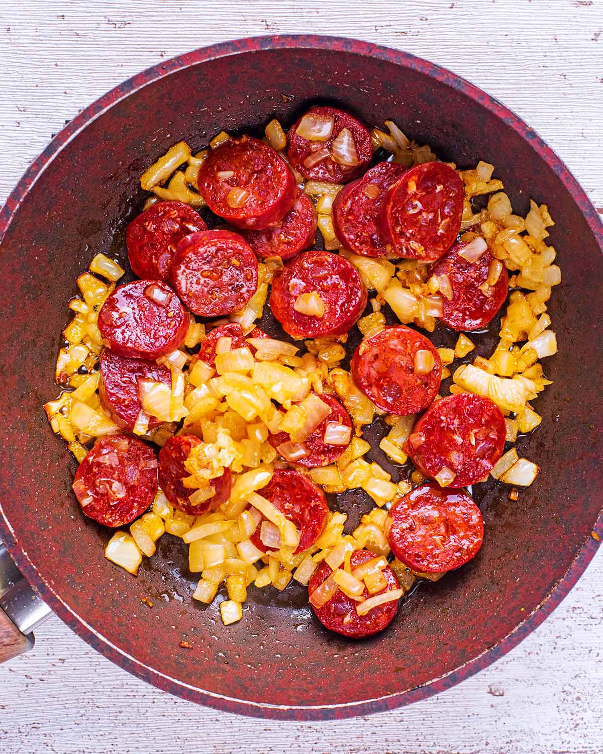 Cooked chorizo and chopped onions in a frying pan.