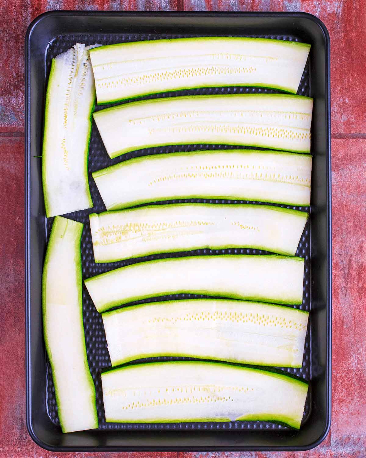 Strips of courgette laid out on a black baking tray.