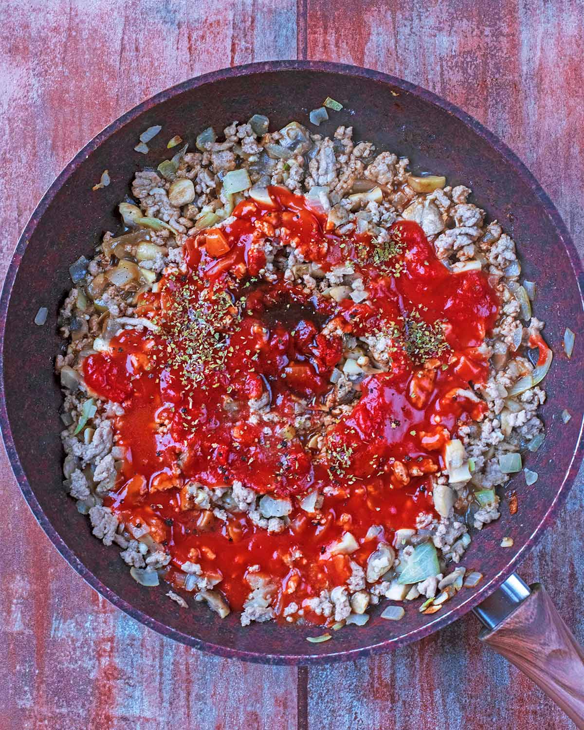 Chopped onion, mushrooms, ground turkey, garlic and pasta sauce in a frying pan.