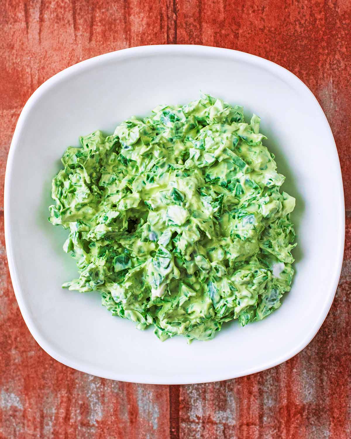 A white bowl containing a mixture of yogurt and chopped spinach.